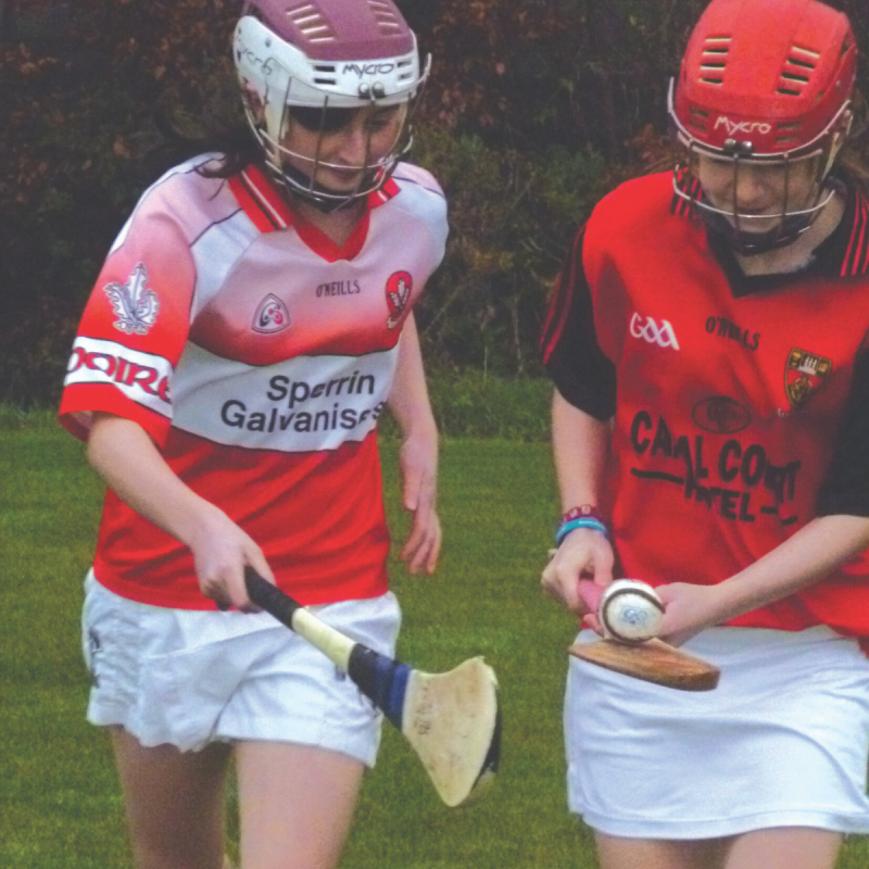 Two girls playing hurling with helmets