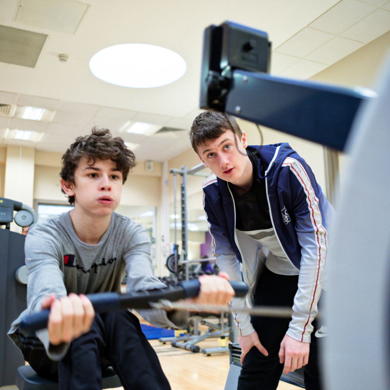 Two young men in gym in rowing machine